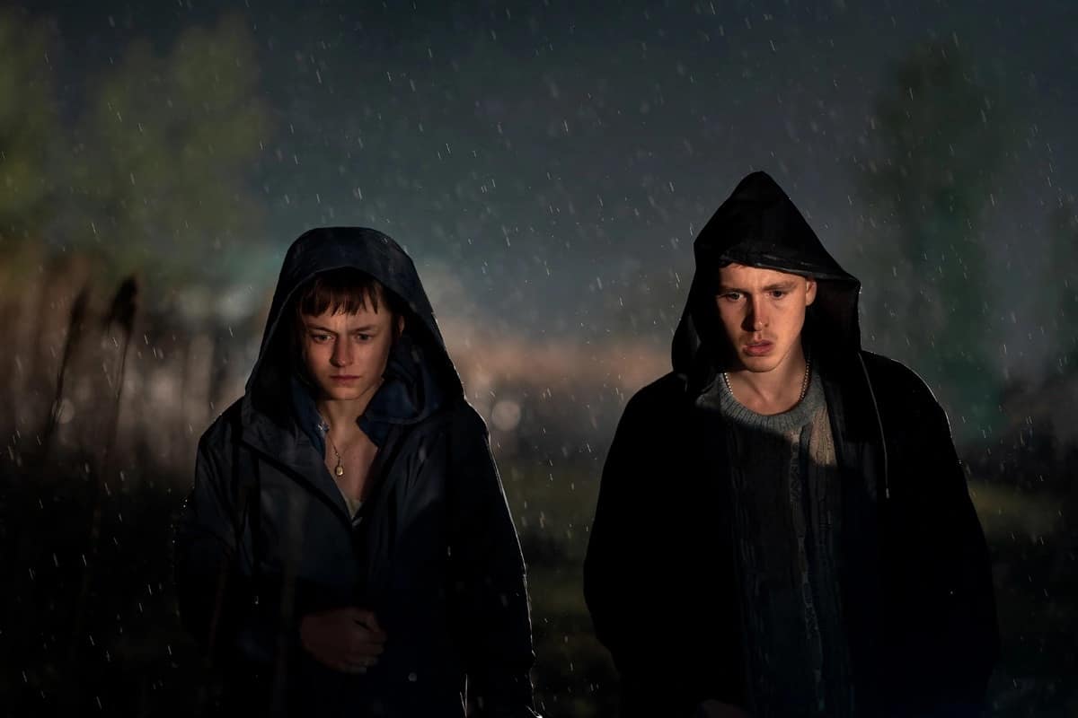 Two people in black coats walk in the rain in this image from FX Productions