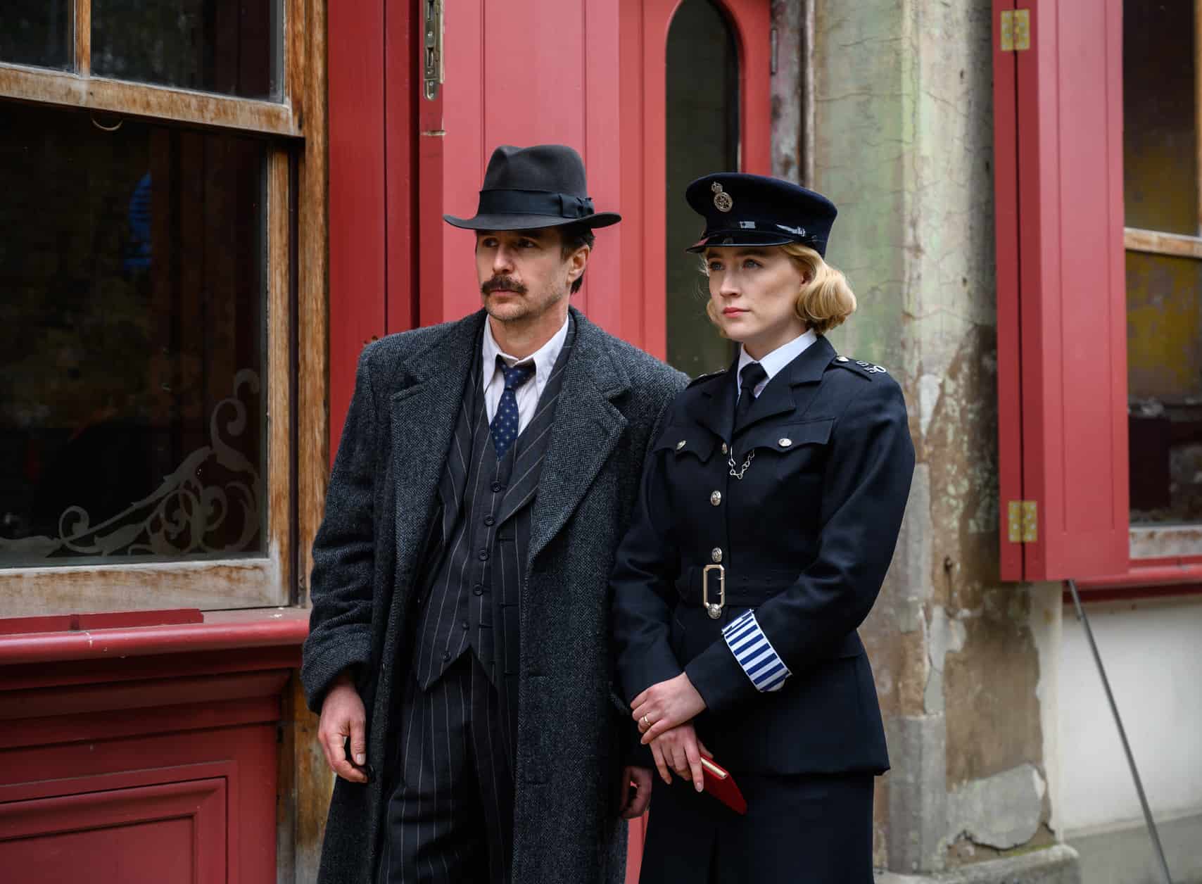 A male inspector and a female officer stand together and look at something off camera