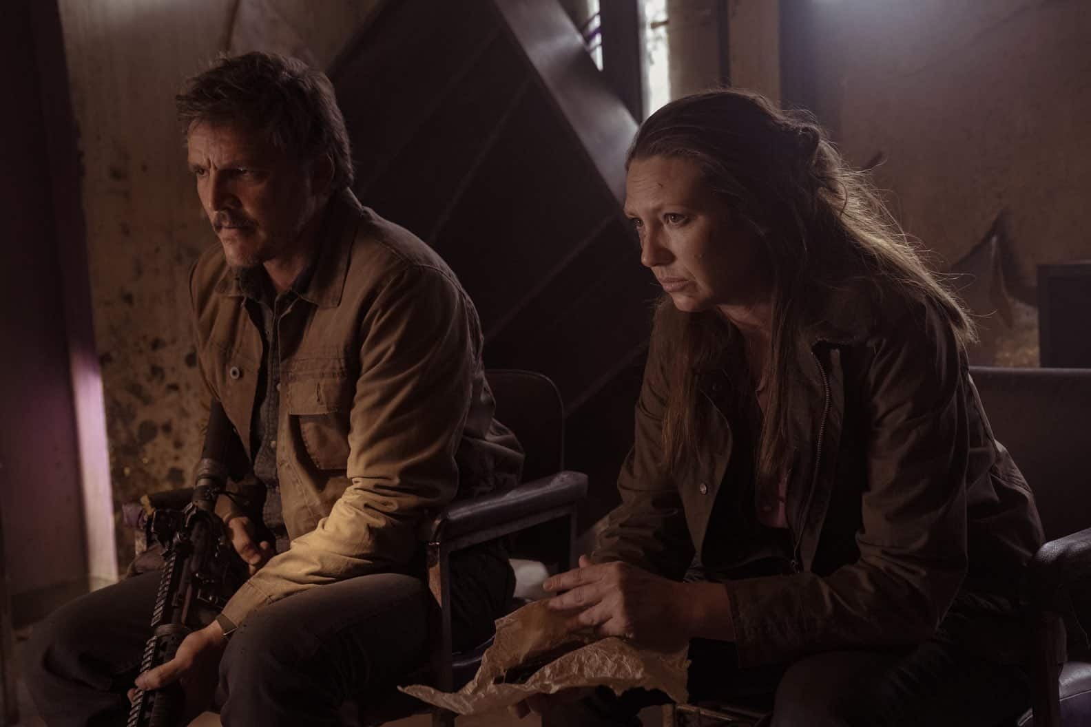 Joel sitting next to Tess holding an automatic rifle