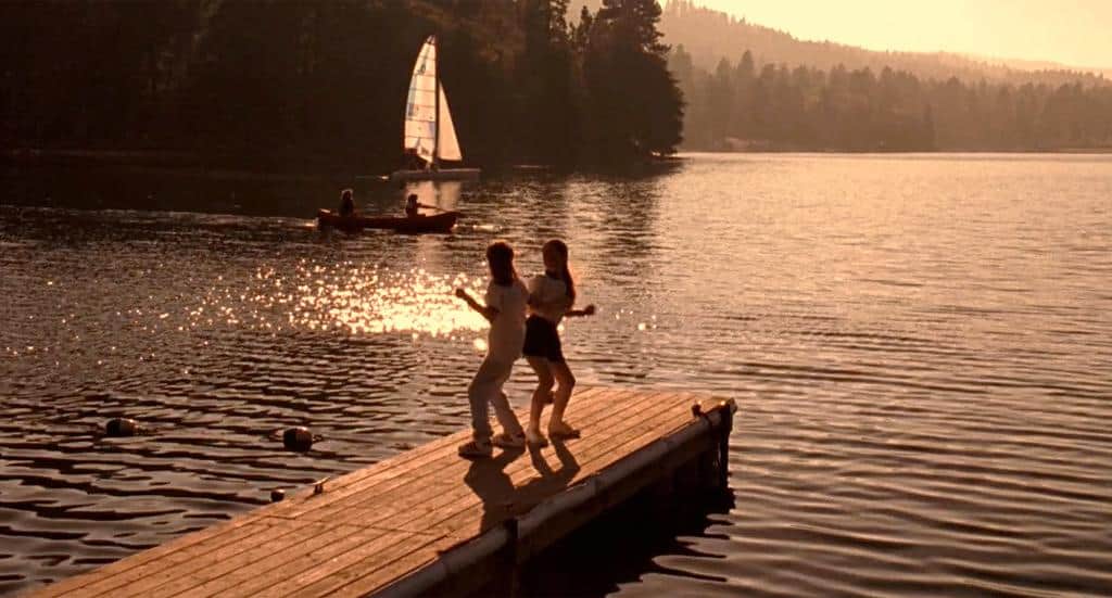 Two girls dancing on a pier in front of a scenic lake