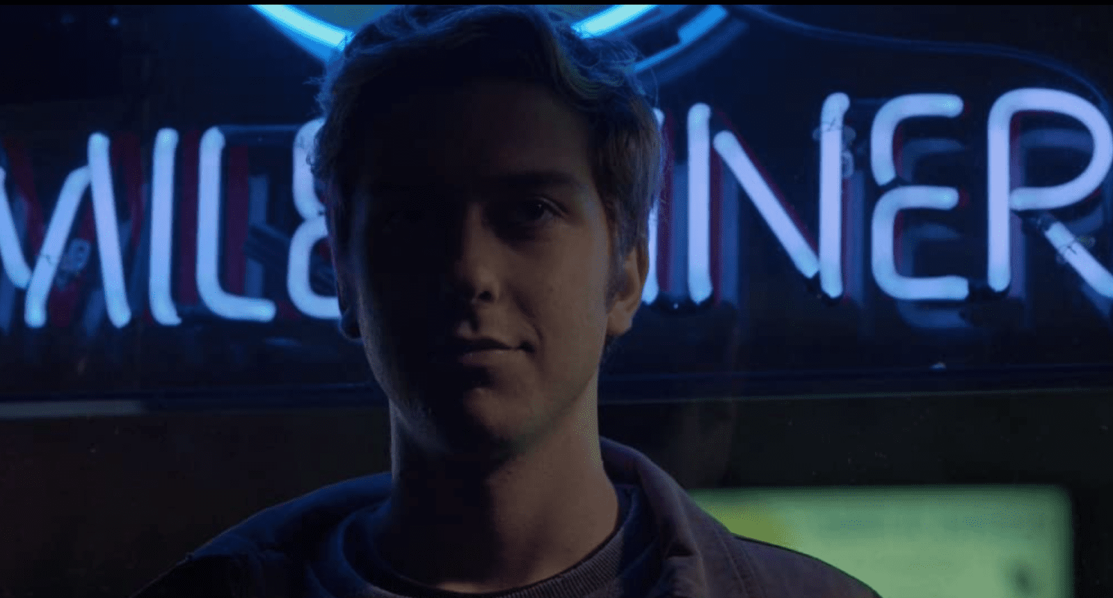 A young man stares mysteriously into the distance while neon lights stand in the background