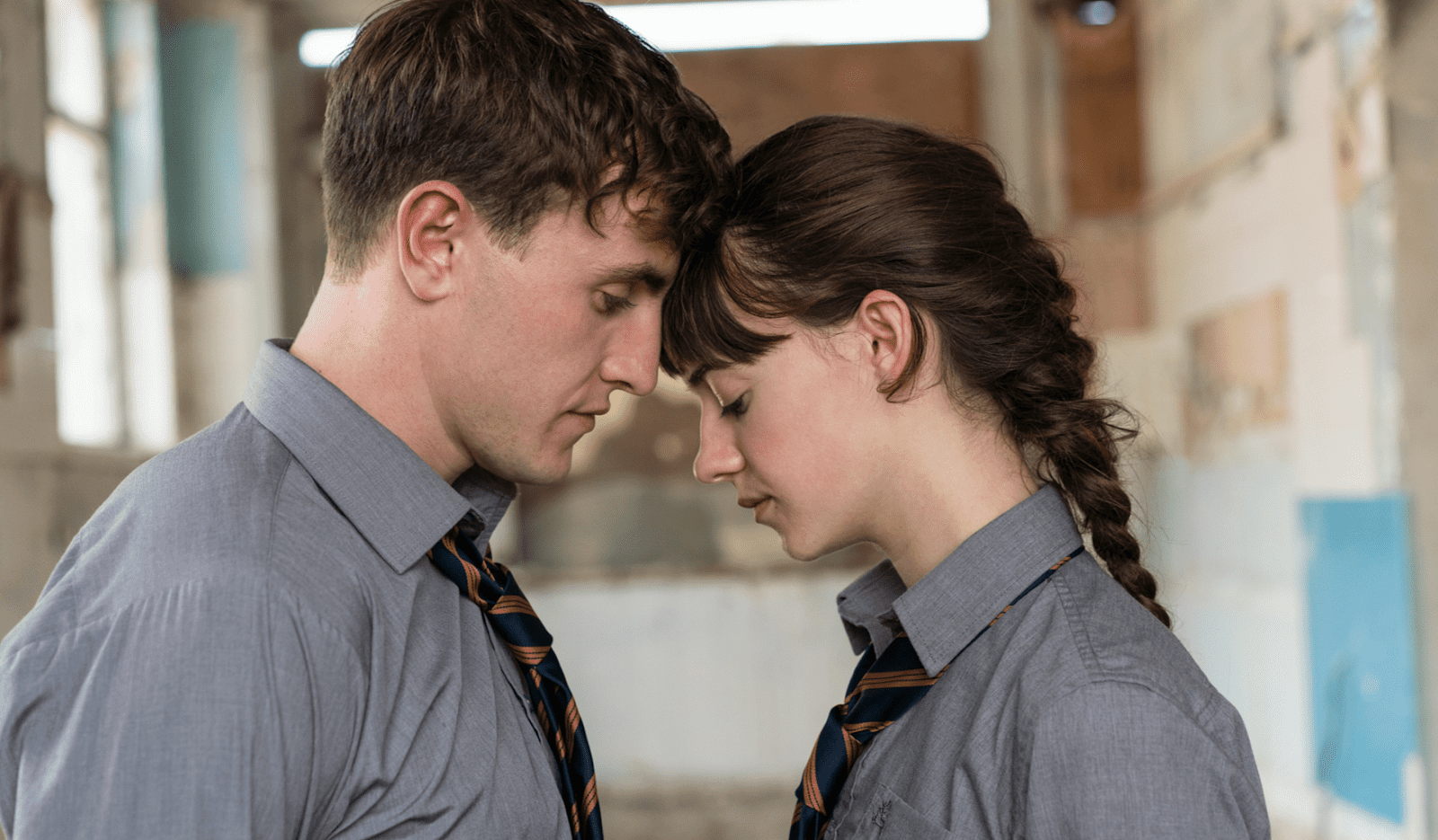 A young man and woman stand in front of each other with their foreheads touching.